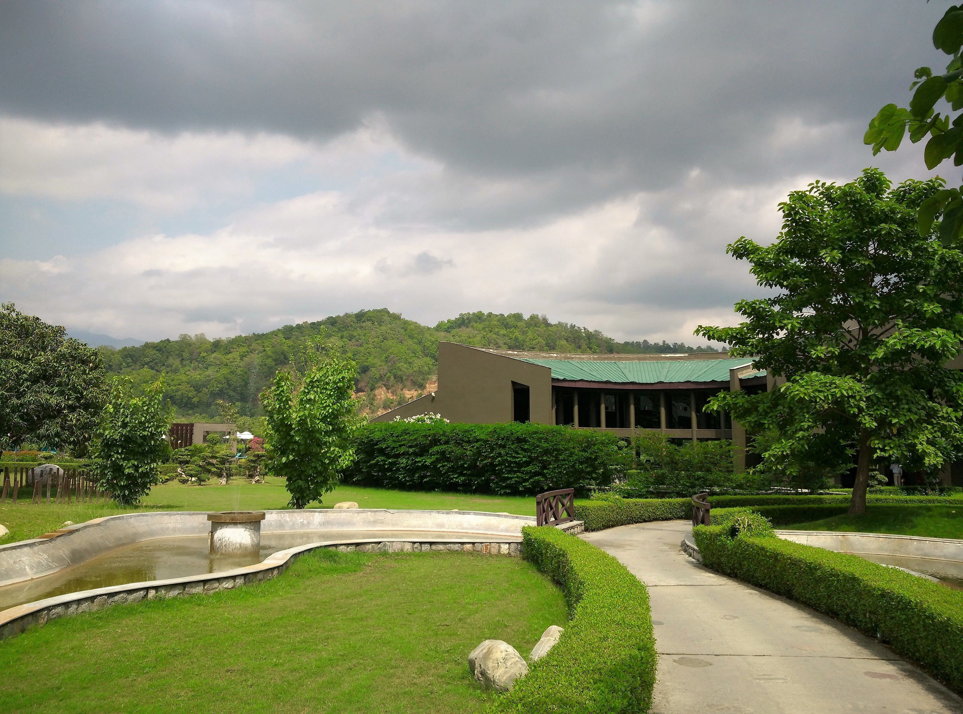 A building with a green roof, surrounded by well-maintained gardens and a curved pathway.