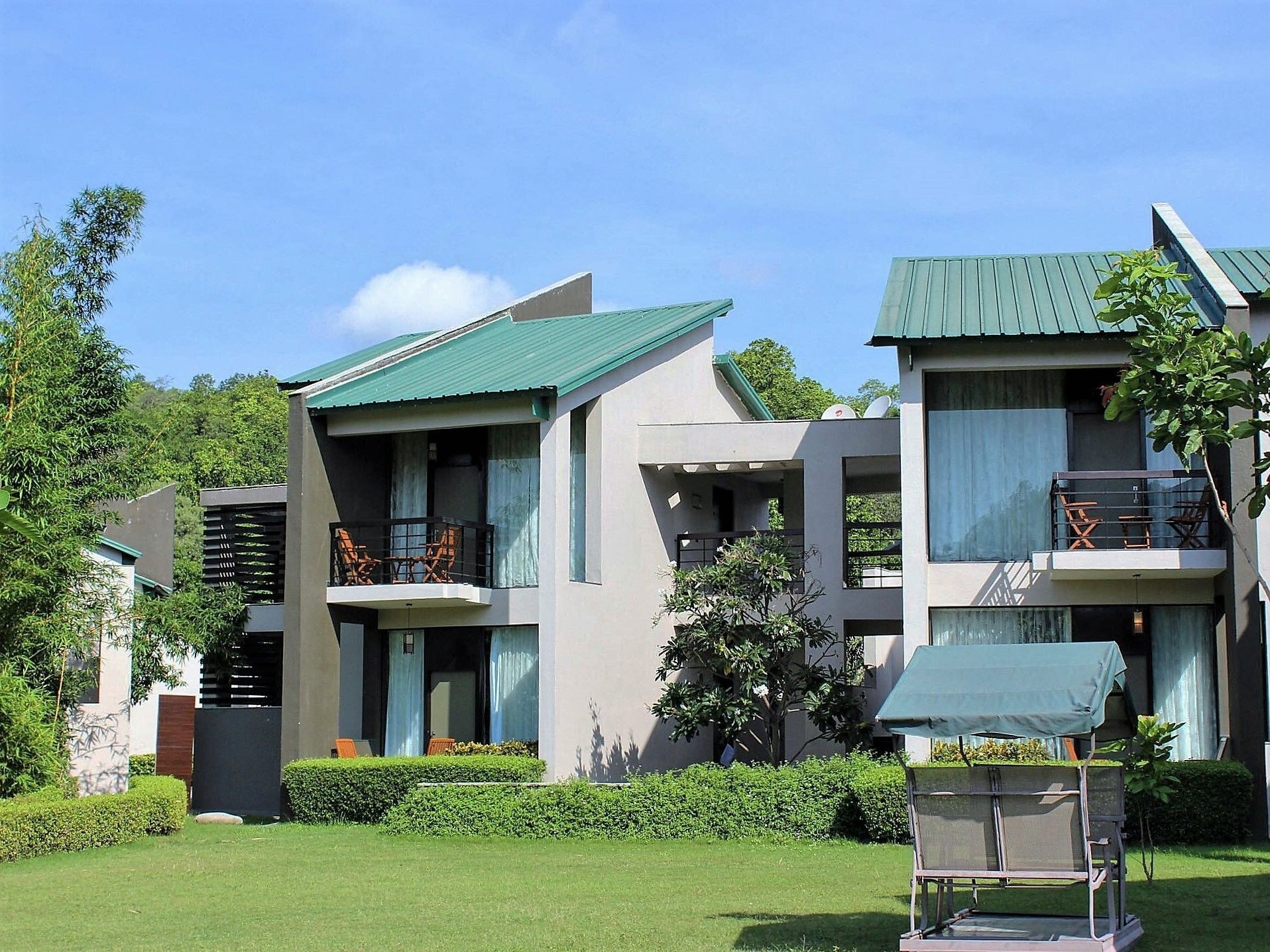 A modern two-story building with balconies, a green roof, and a well-maintained garden.