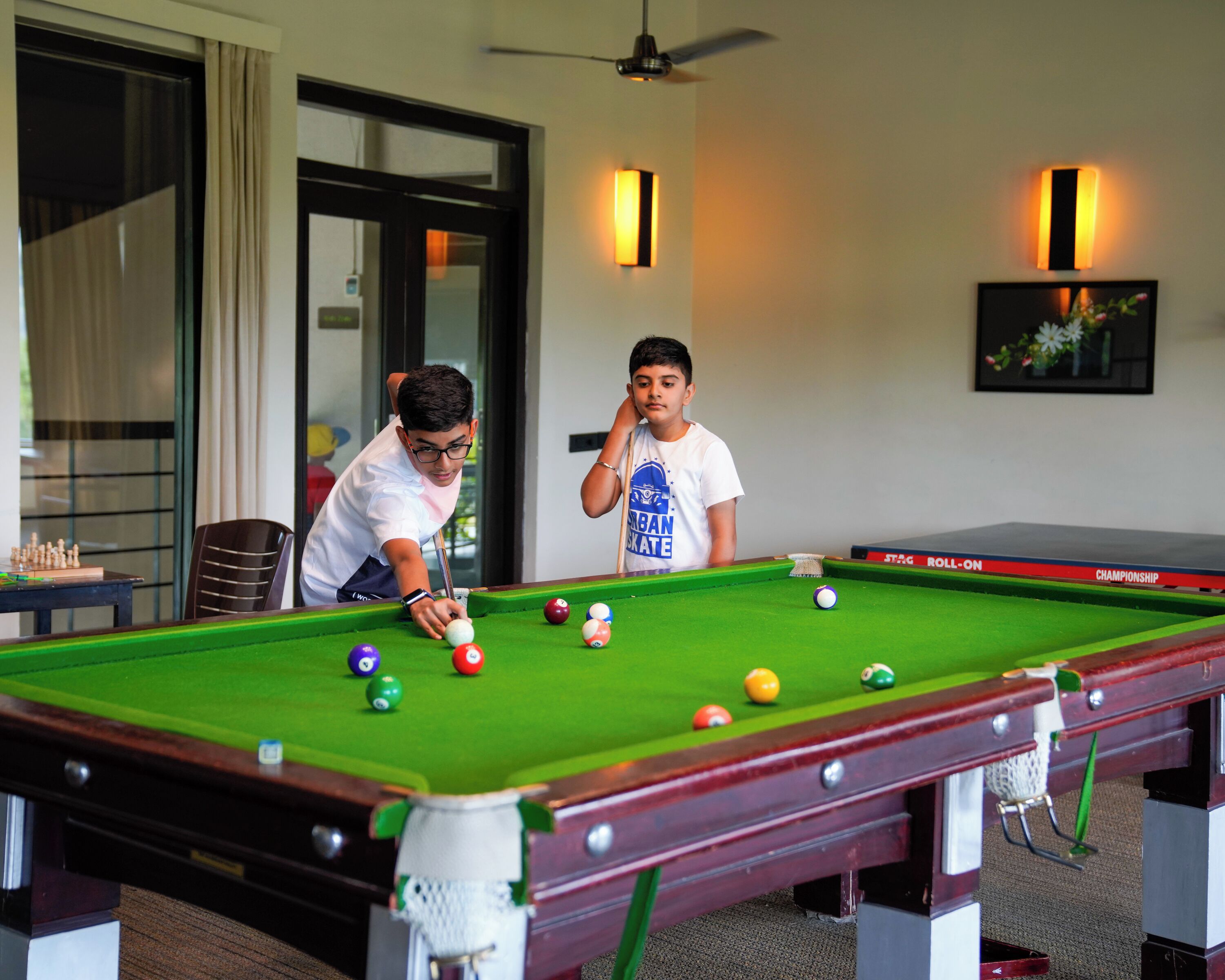 A pool table with balls, a ceiling fan, and two people playing.