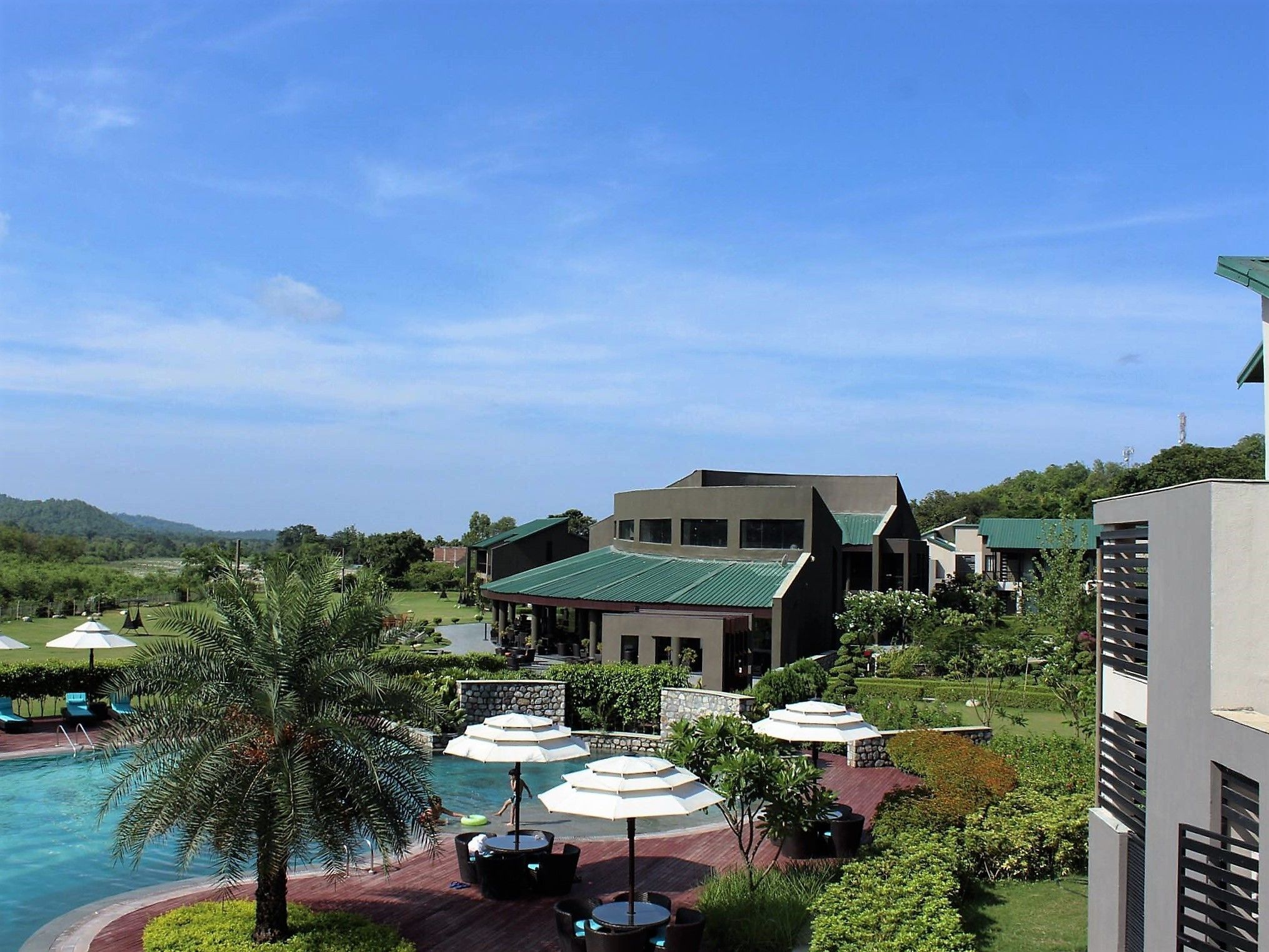 A resort with a swimming pool, outdoor seating, and a large building with a green roof.