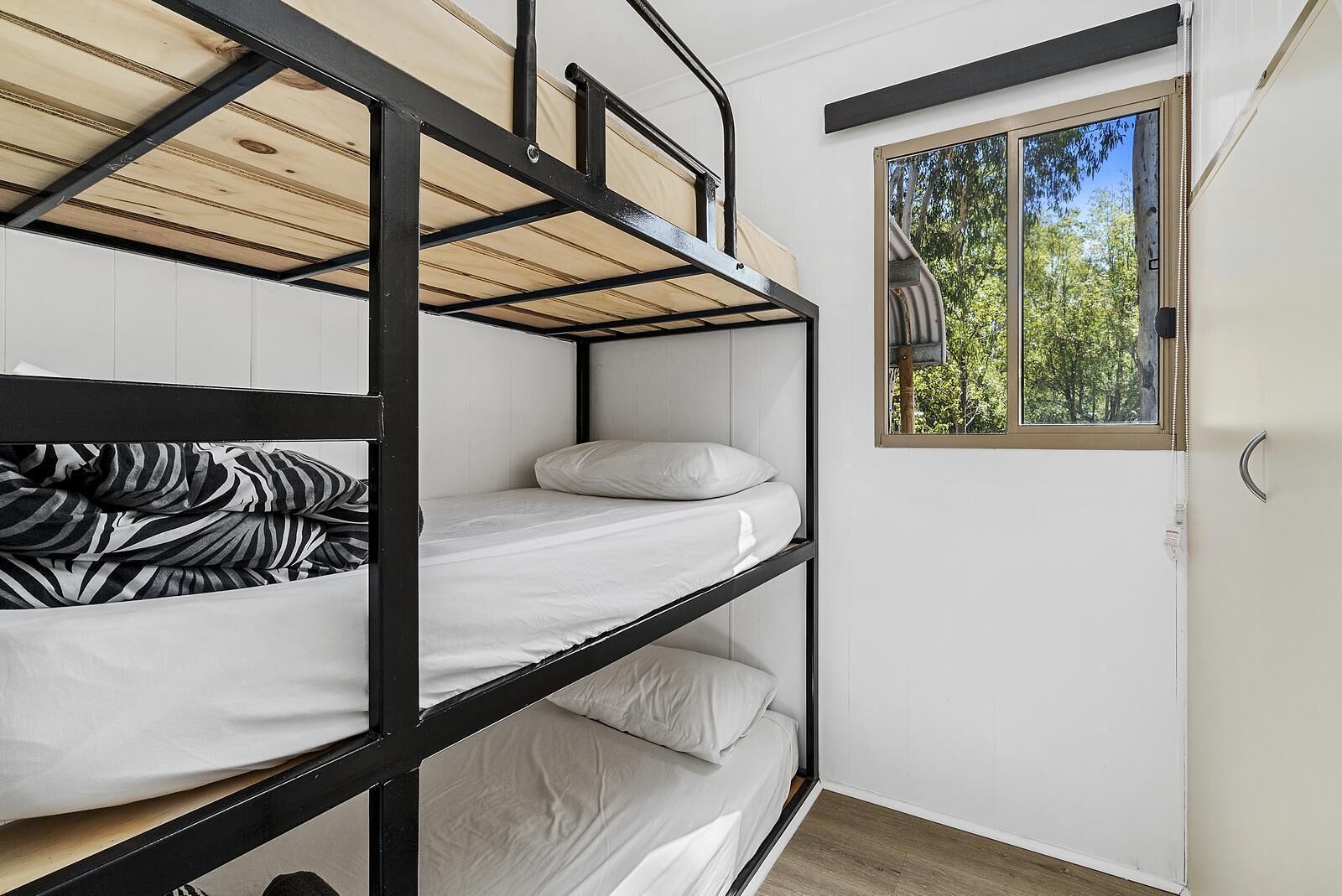 A bunk bed room with a window providing a view of trees.