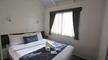A neatly made bed with white linens, a dark blue blanket, and two rolled towels.