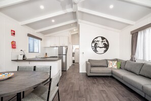 Una sala de estar moderna con un sofá gris, una mesa de comedor con sillas y una cocina al fondo.