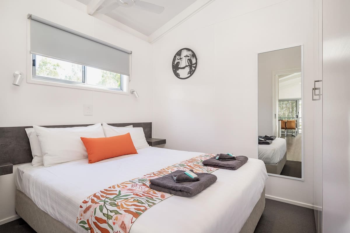 A hotel room with a bed, a window, a wall-mounted artwork, and a mirror.
