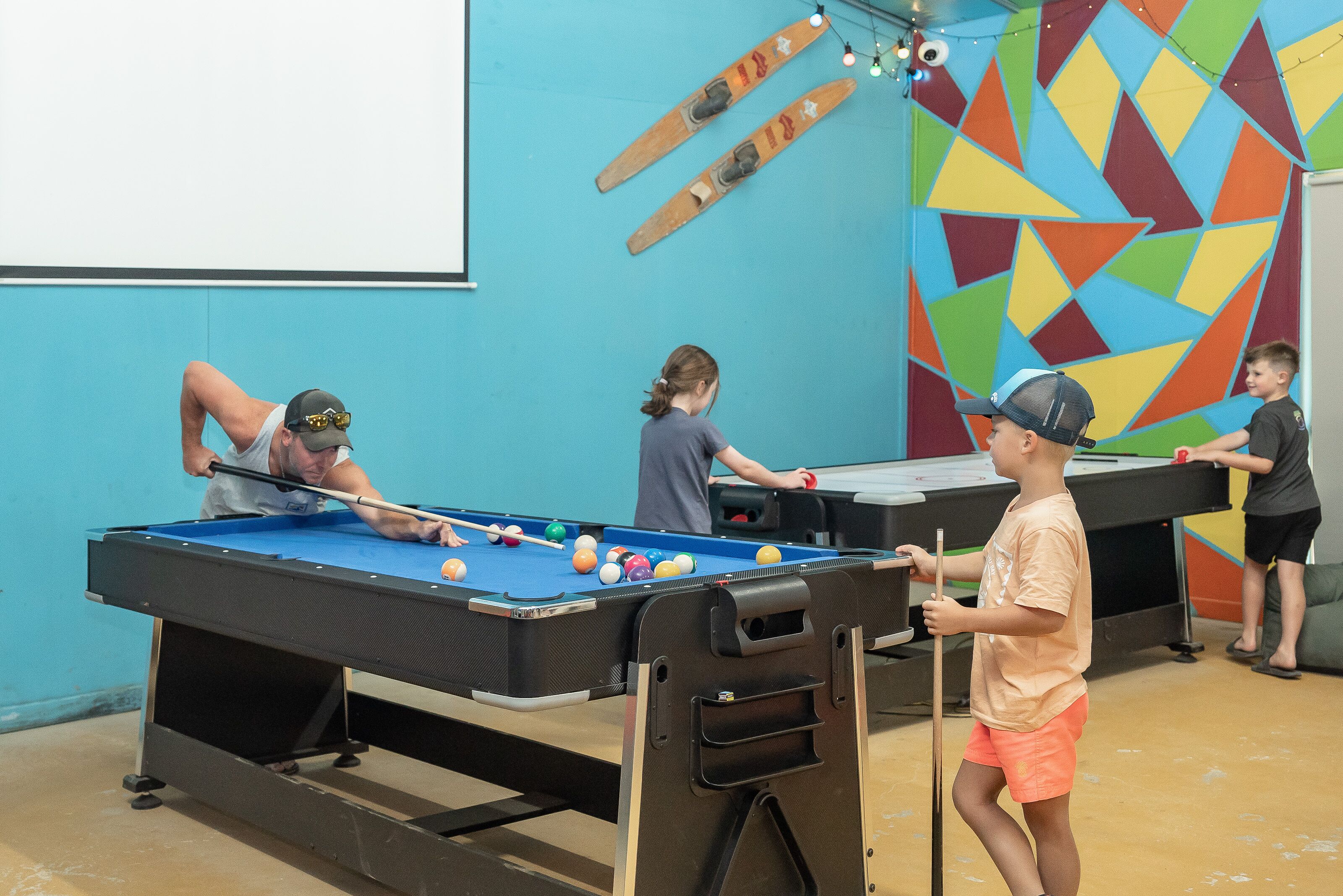 Une table de billard dans une pièce dont le mur est décoré de motifs géométriques aux couleurs vives.