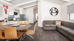 A modern kitchen with a dining area, a gray sofa, and a wall art piece.