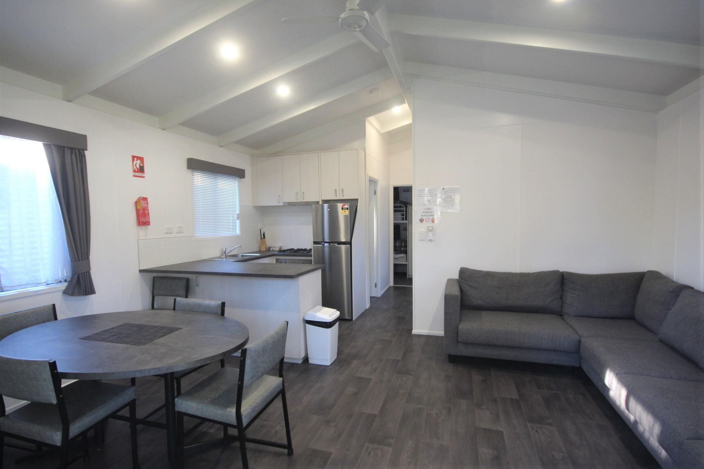 A modern kitchen with white cabinets, a stainless steel refrigerator, and a dining area with a round table and chairs.