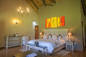A bedroom with a bed, bedside tables, a chandelier, artwork on the wall, and a ceiling fan. - Chrislin African Lodge (Addo)