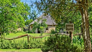 A reception area with a sign, surrounded by lush greenery and a thatched-roof building. - Chrislin African Lodge (Addo)