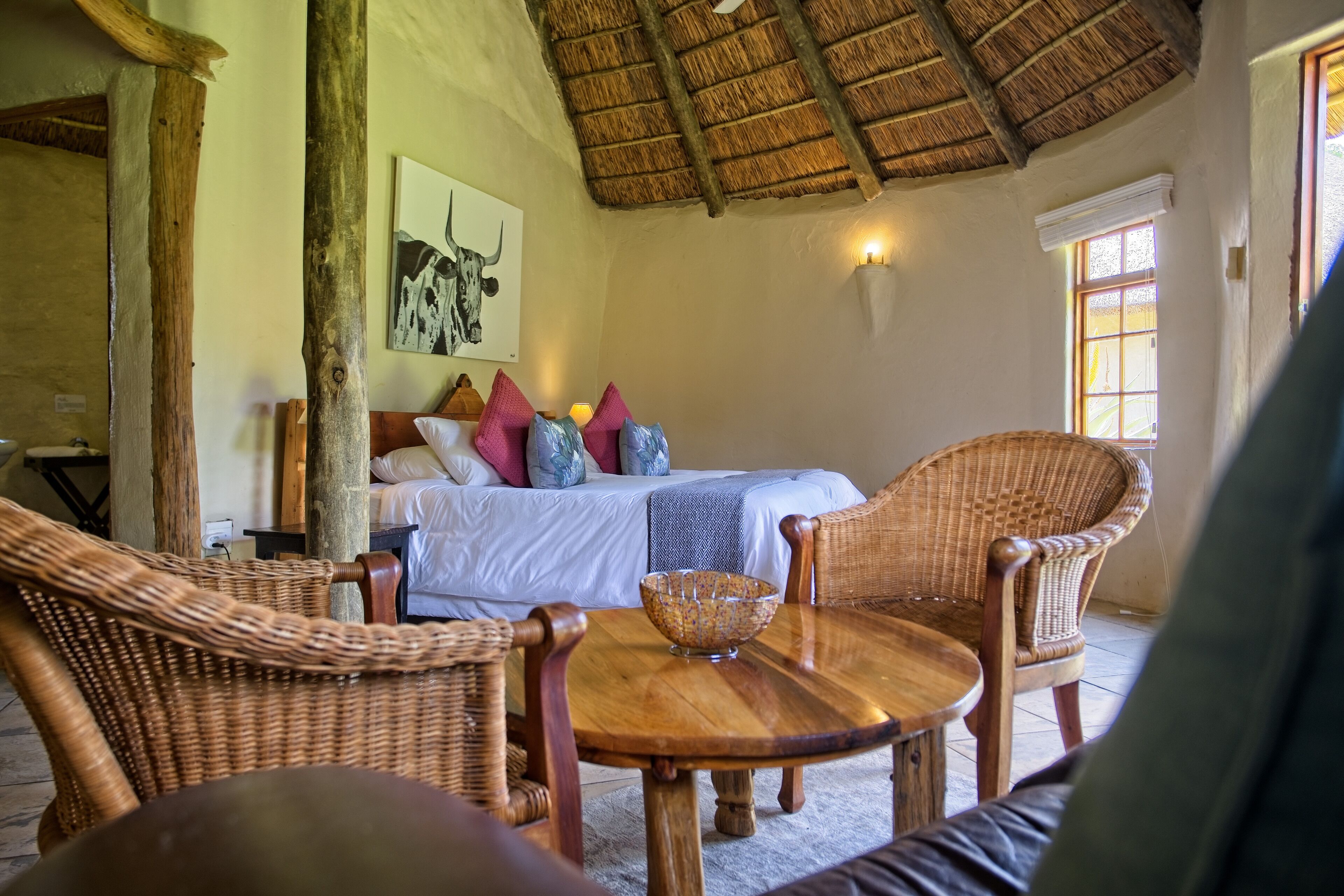 Een kamer met een bed, rieten stoelen, een houten tafel en een rieten plafond.