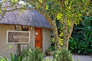 A rustic hut with a thatched roof and a 'RECEPTION' sign, surrounded by lush greenery.