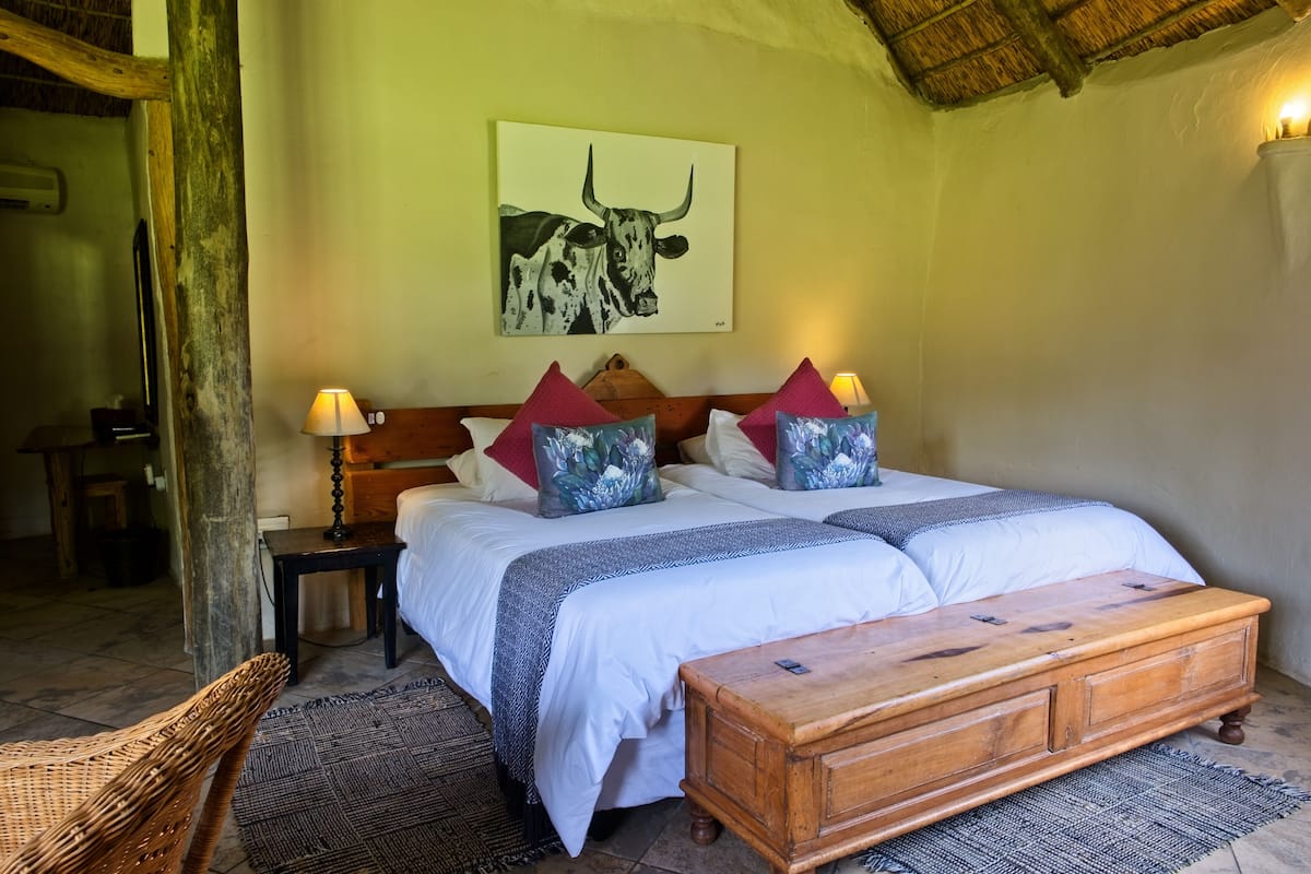 A bedroom with a bed, pillows, a nightstand, a wooden bench, and a wall painting.