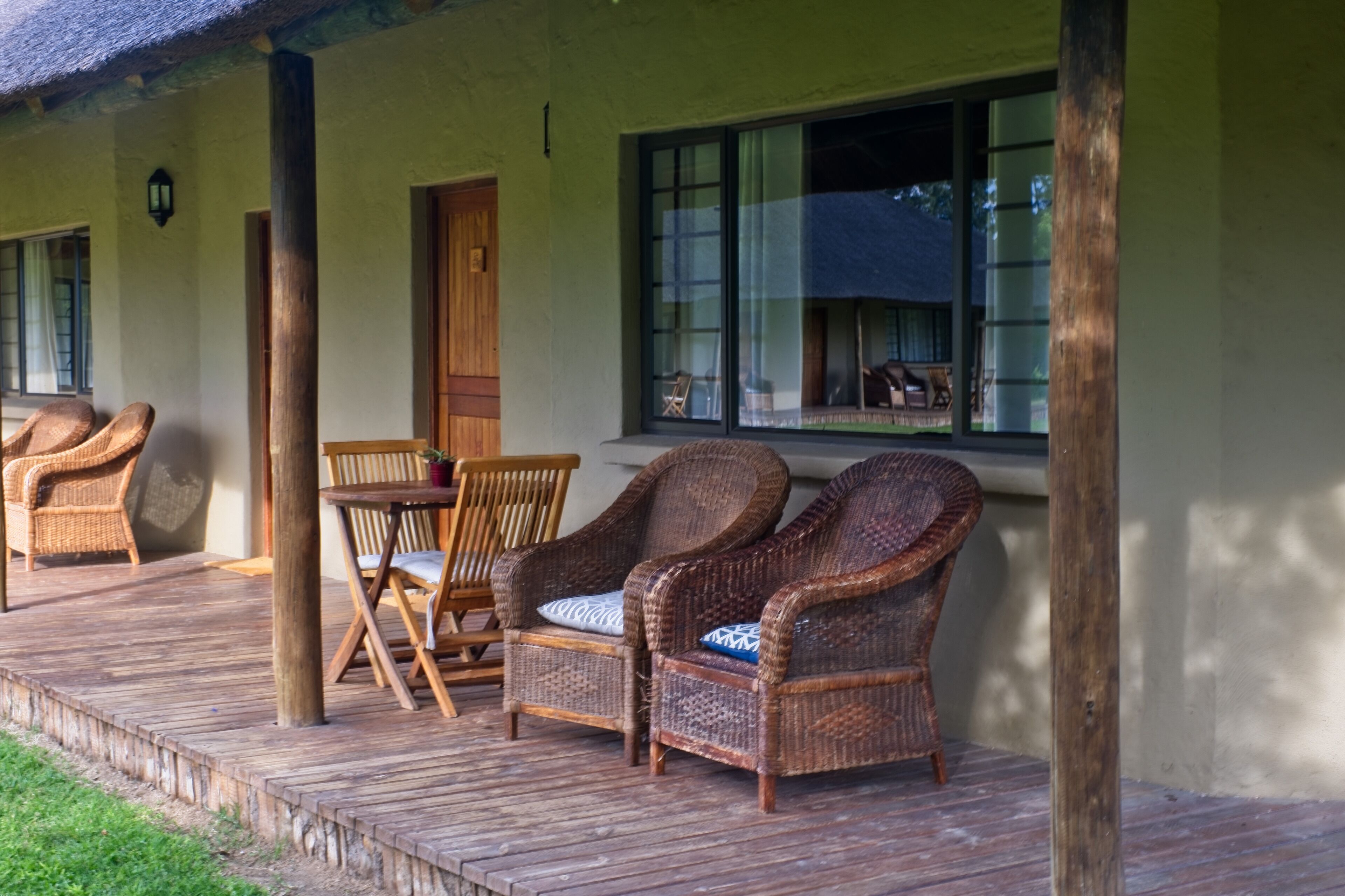 Una terraza de madera con mobiliario de mimbre, incluyendo dos sillas y una mesa.