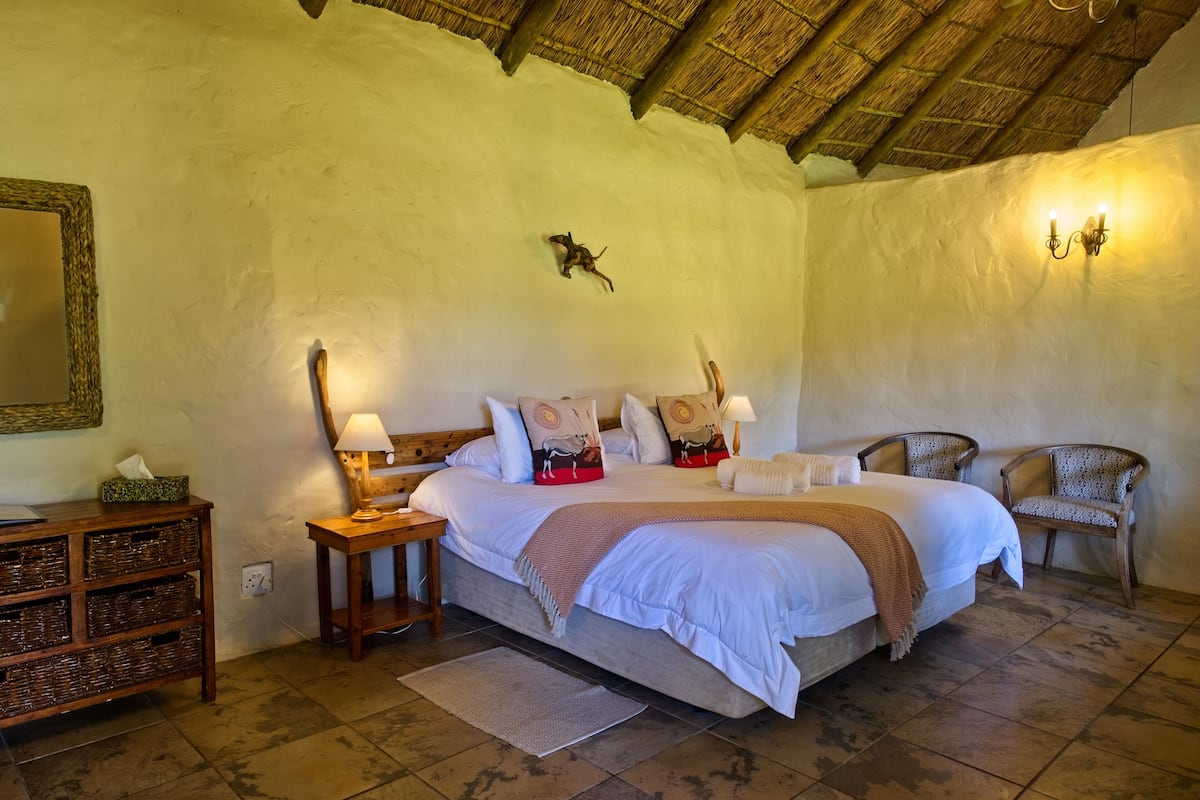 A bedroom with a large bed, bedside tables, a nightstand, a mirror, and a wall-mounted lamp.