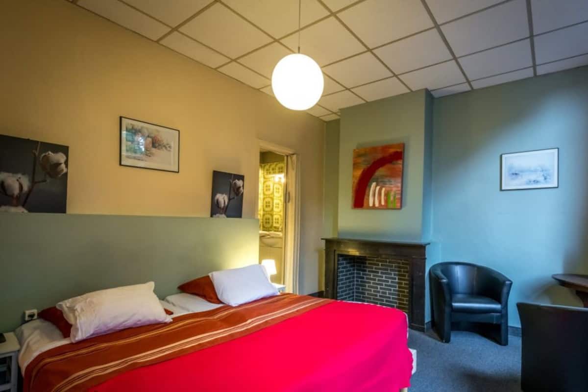 A hotel room with a bed, a fireplace, a chair, and artwork on the walls.