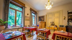 A dining area with tables set for four, a chandelier, and a view of greenery outside. - Hotel Ensor (Bruges)