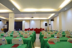 Uma sala de conferências com mesas dispostas em fileiras, cada uma com toalha verde e garrafas de água.