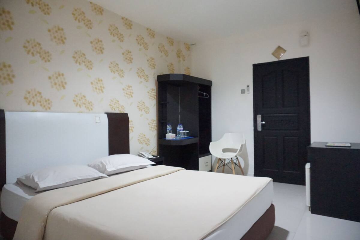 Une chambre d’hôtel avec un lit, un bureau, une chaise et une armoire.