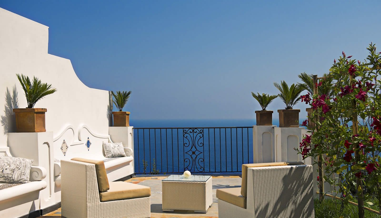 A terrace with white furniture, a blue gate, and potted plants.