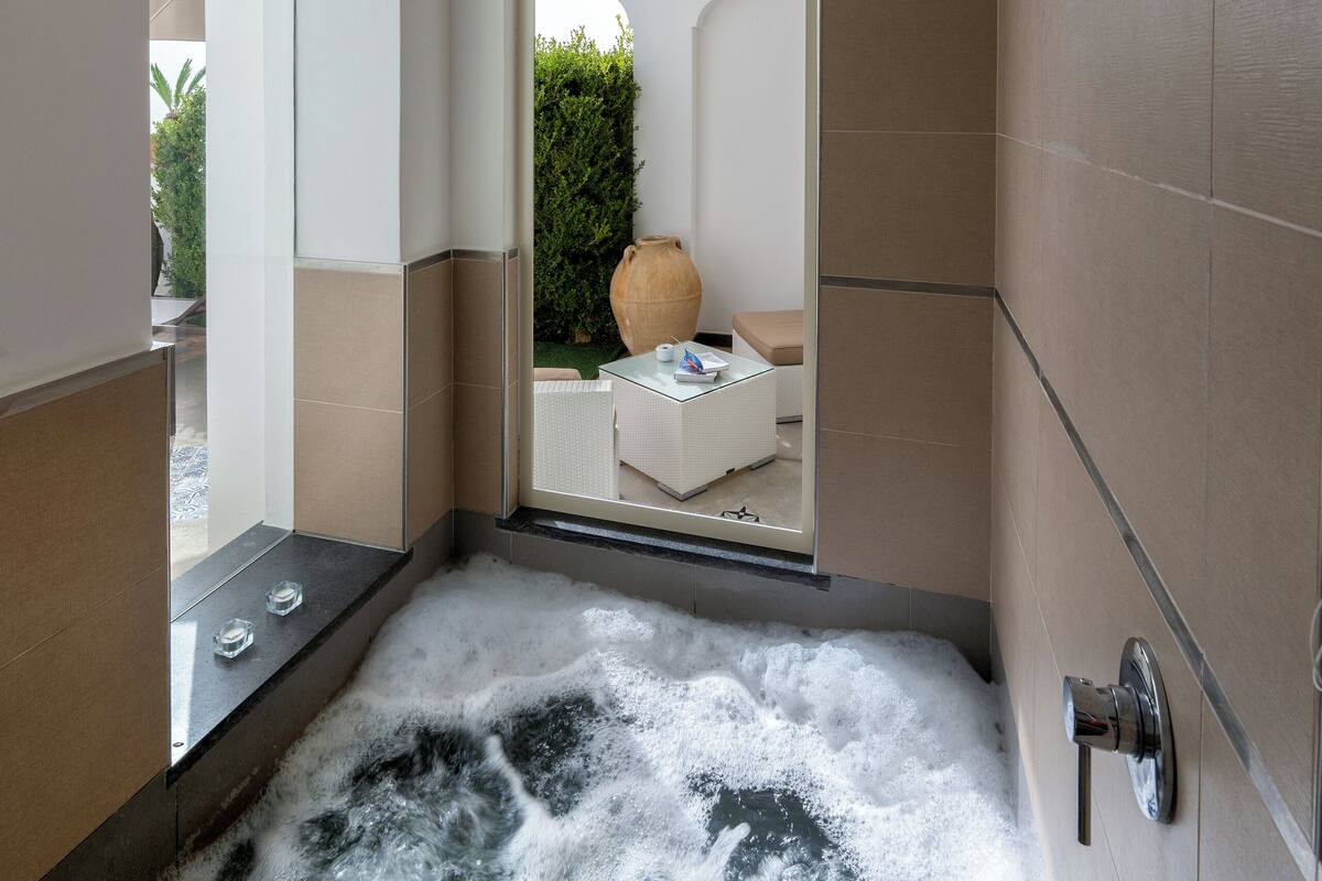 Een moderne badkamer met een groot bad, een douchecabine van glas en uitzicht op een tuin.