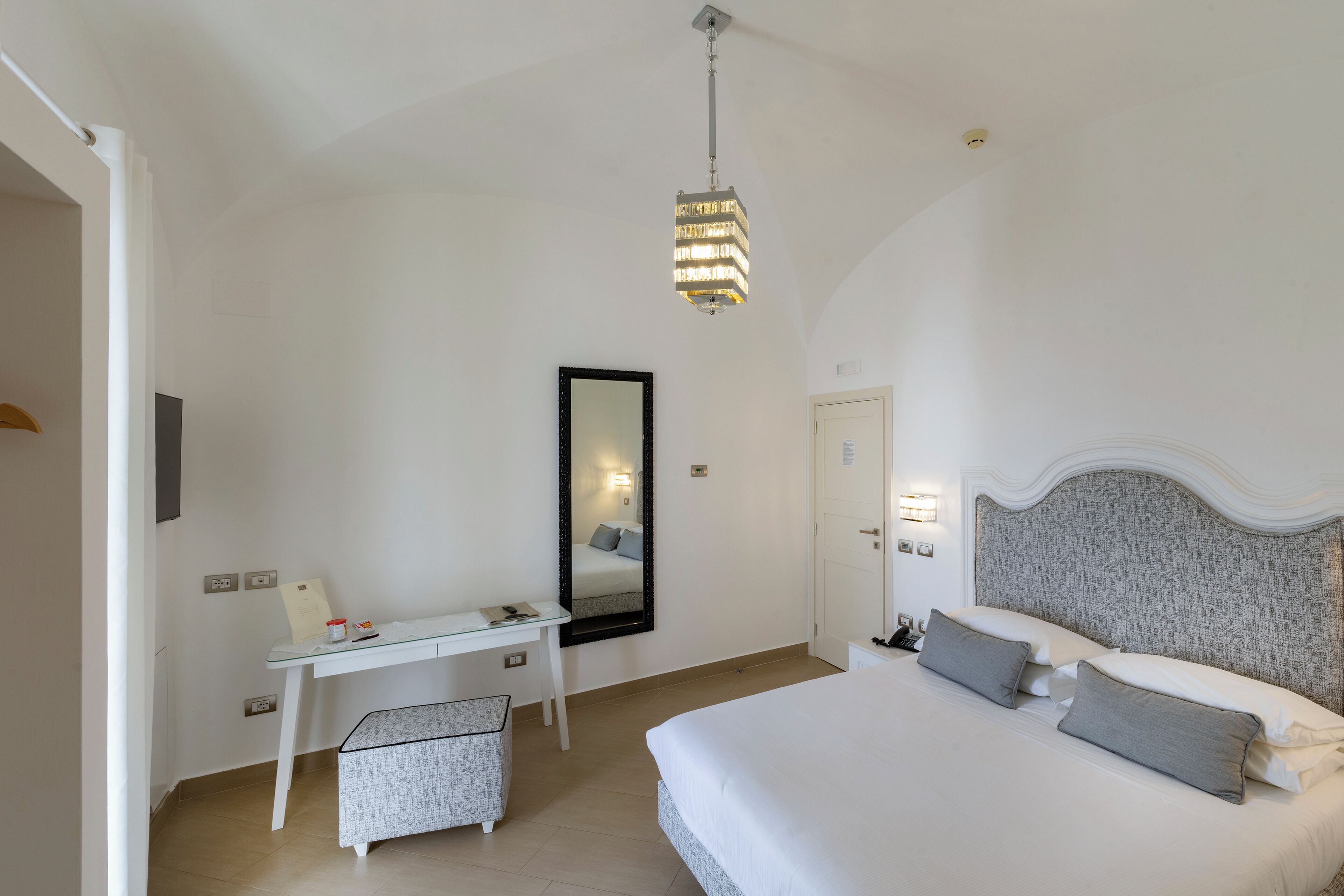 A bedroom with a bed, bedside table, desk, chair, and a mirror.