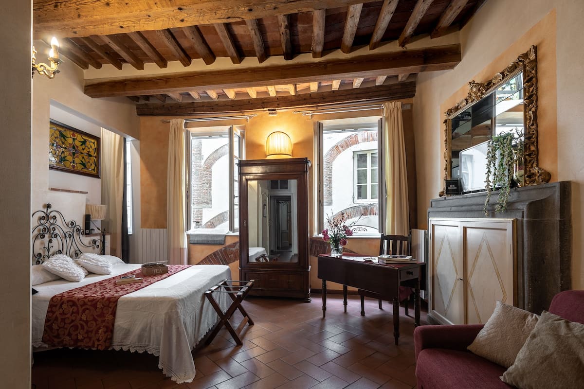 A bedroom with a bed, a desk, a chair, a mirror, and a fireplace.
