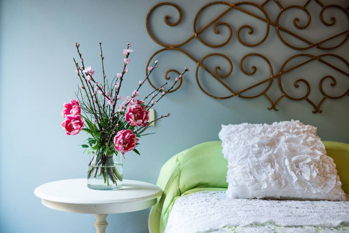 A room with a round white table holding a vase of pink flowers, a green upholstered chair, and a white pillow on a green sofa.