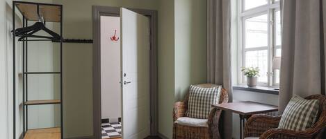 A room with a wooden floor, a white door, wicker chairs, a small table, and a window with curtains.