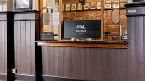A reception area with a checkered floor, wooden paneling, and a large arched window displaying framed pictures and a vintage camera. - Stationen Bed & Breakfast (Ystad)