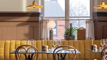 En restaurang med ett rutmönstrat golv, trästolar, en sittgrupp med bänkar och hängande taklampor.