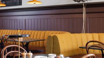Un interior de restaurante con un largo banco de madera, mesas redondas y sillas.