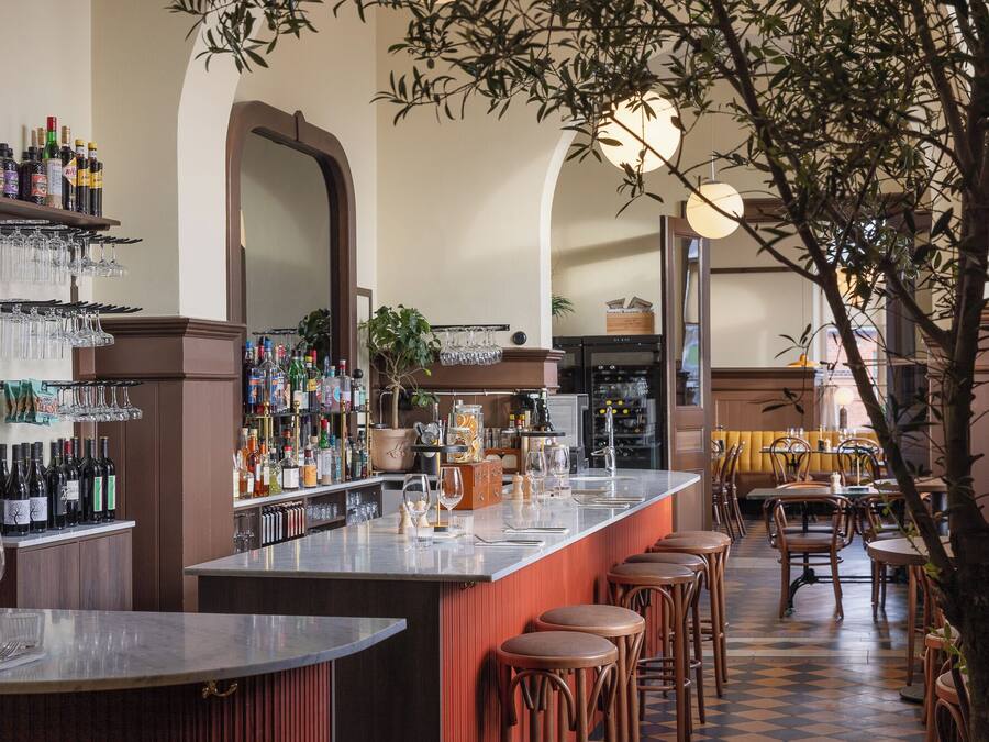 Una zona de bar con una barra larga, taburetes y una variedad de botellas y vasos.