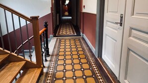 A hotel hallway with a patterned floor, a wooden staircase, and a door with a number. - Stationen Bed & Breakfast (Ystad)