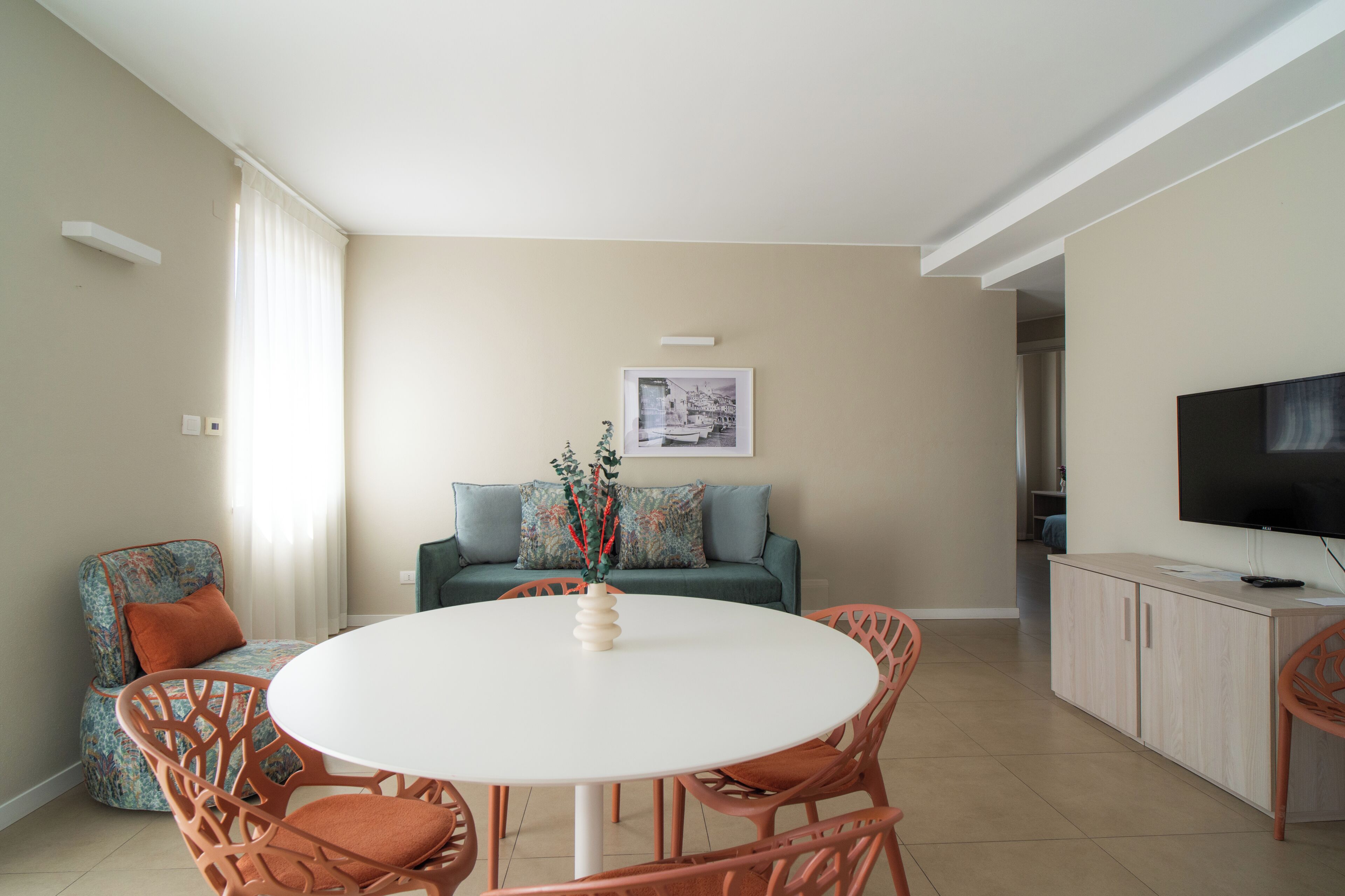 A living room with a round table, orange chairs, a sofa, and a television.