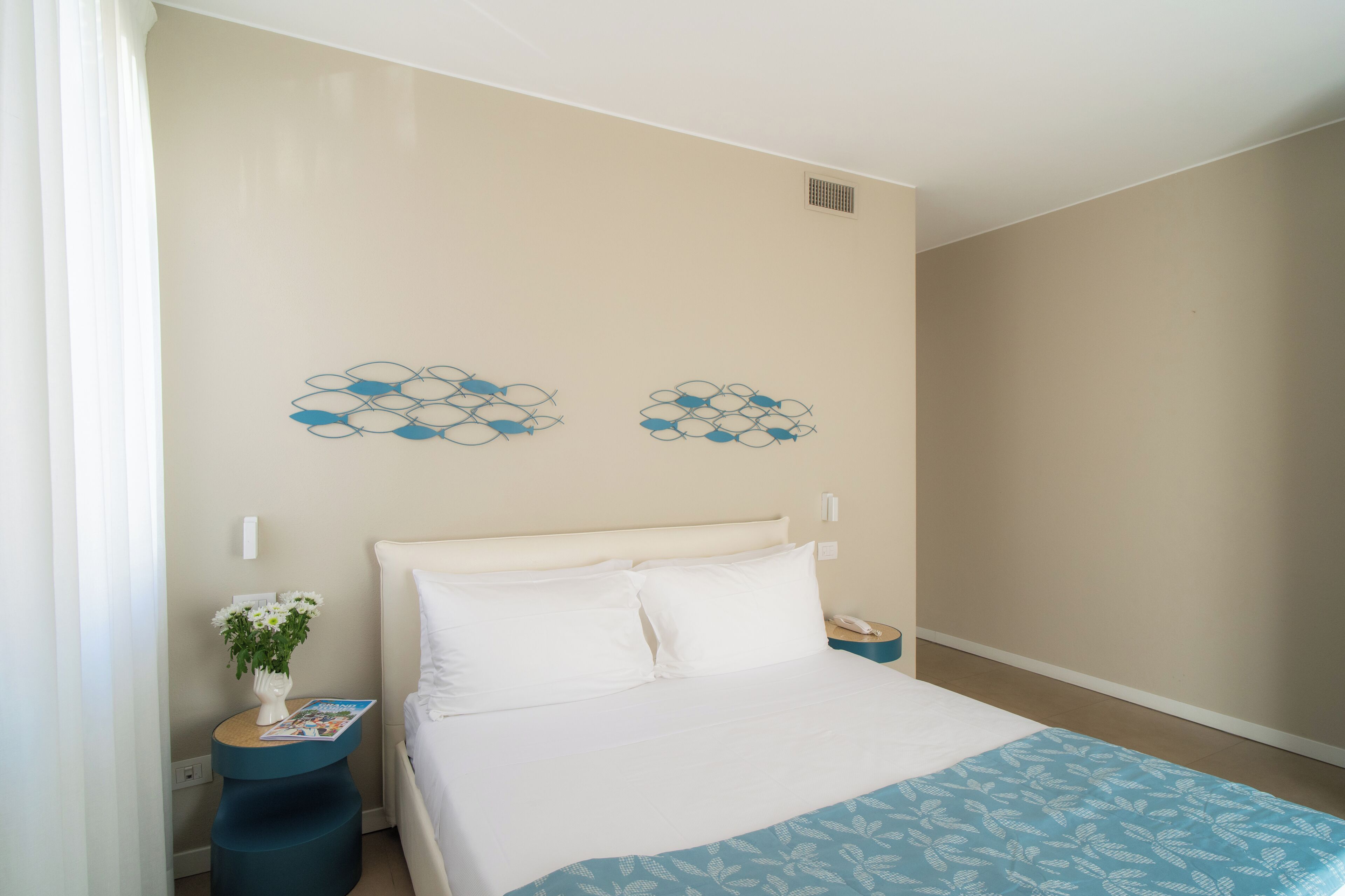 A bedroom with a bed, a nightstand, a vase with flowers, and wall art.