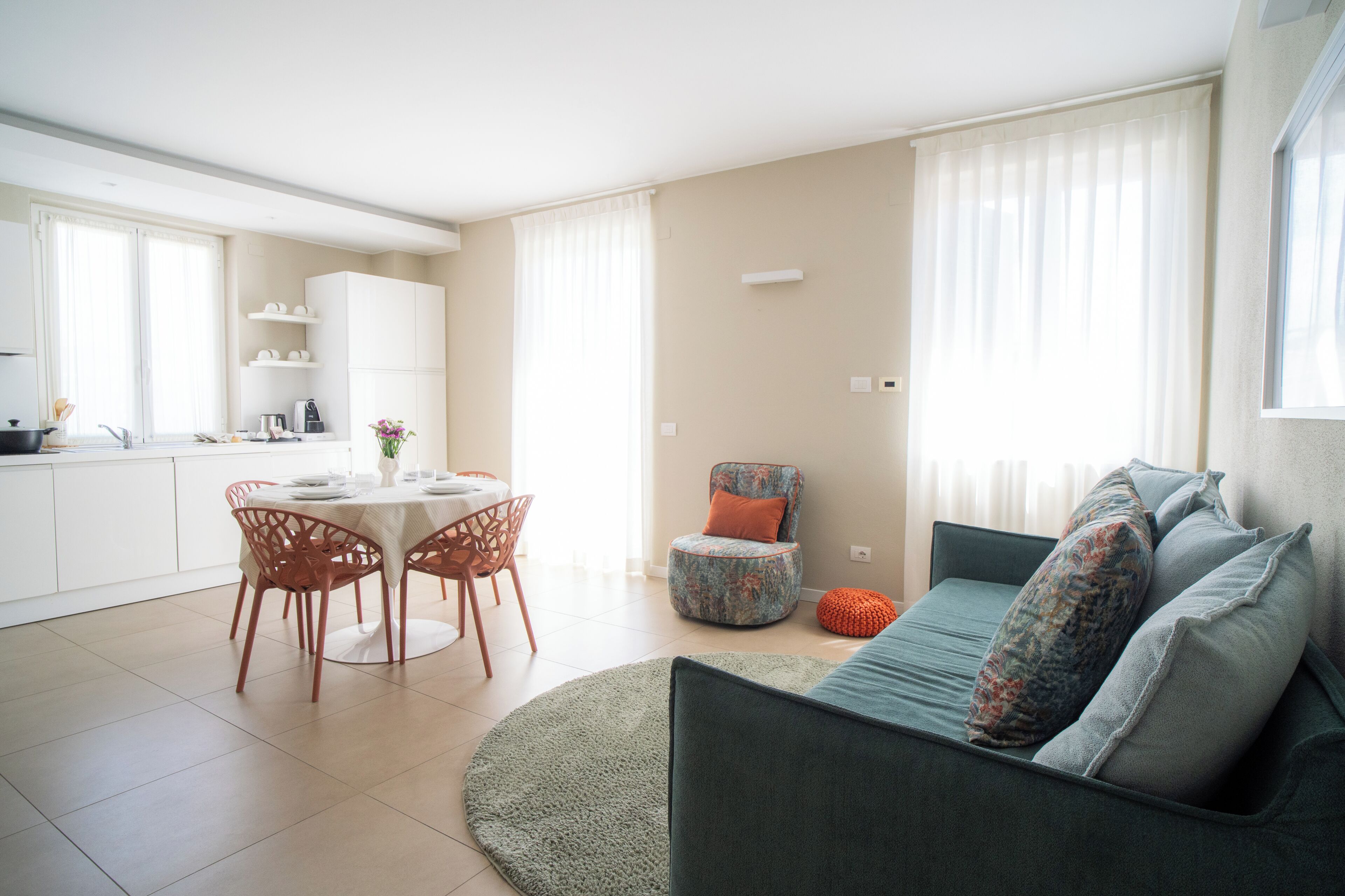 Una sala de estar moderna con un sofá, una mesa de comedor con sillas, una zona de cocina y un ventanal con cortinas.
