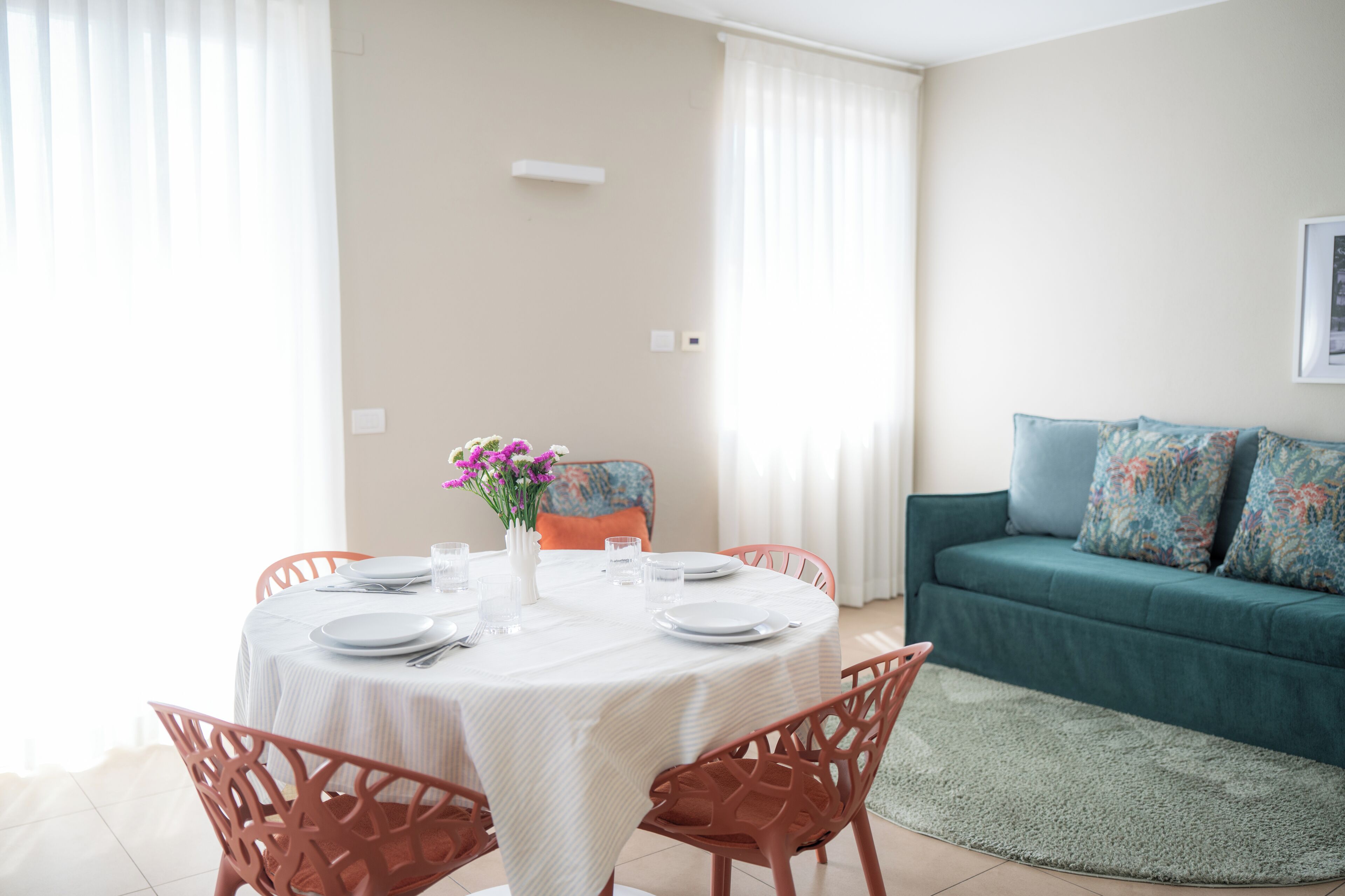 A dining area with a round table set for four, a sofa, and a window with curtains.