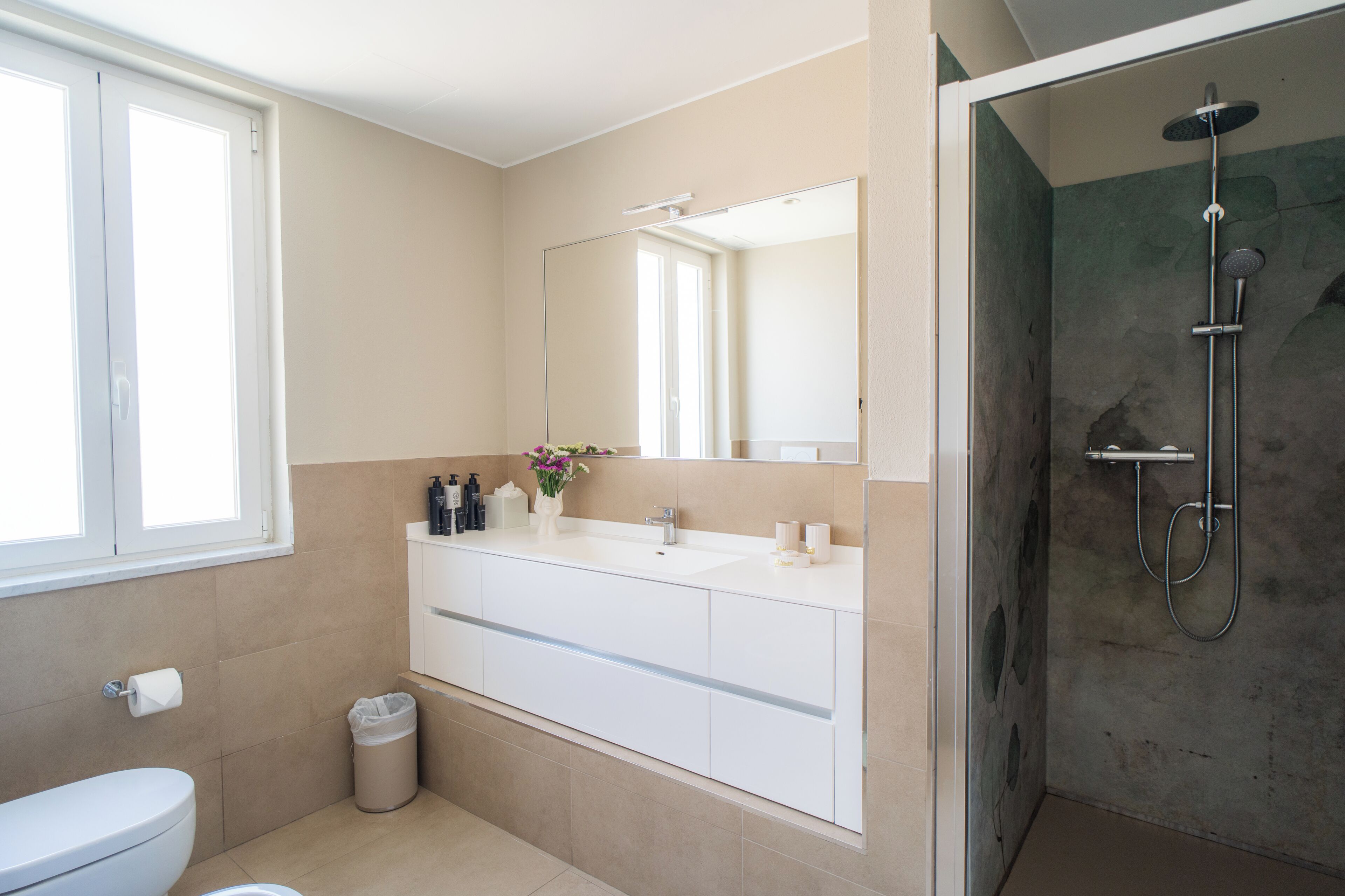 Un baño con inodoro, lavamanos con espejo y zona de ducha.