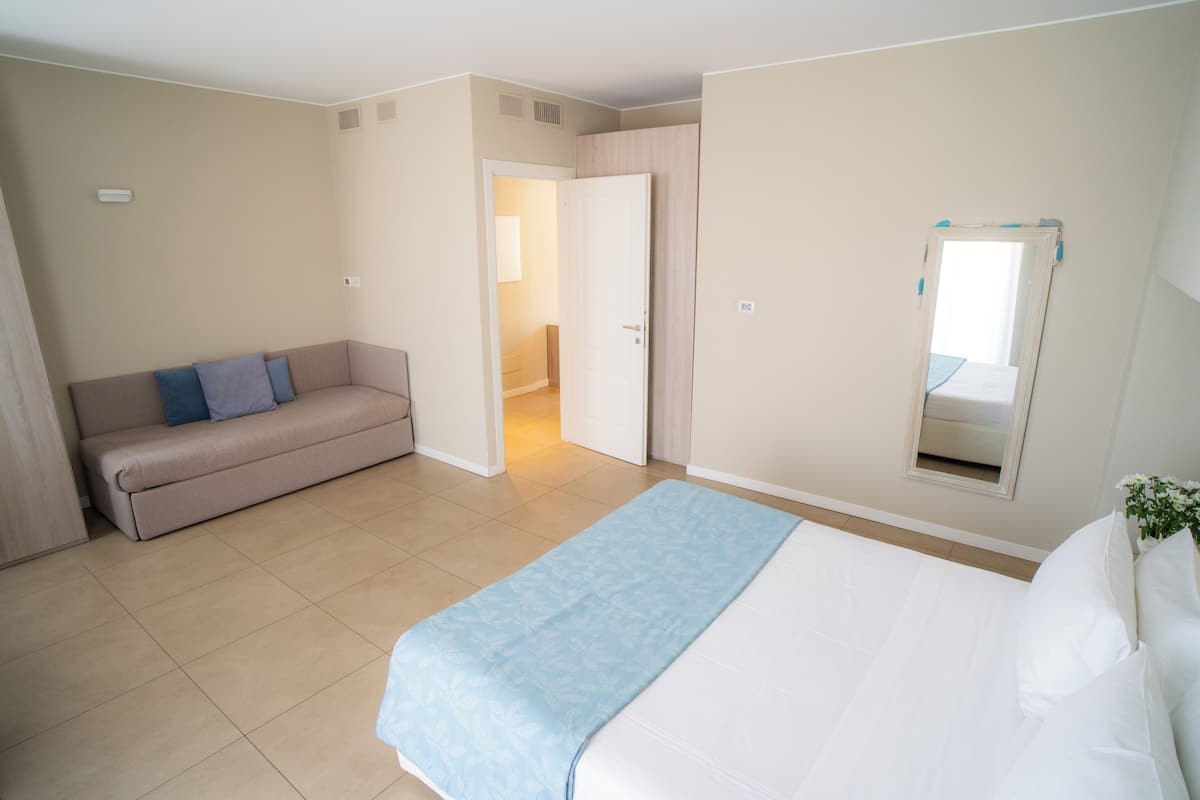 Une chambre d’hôtel avec un lit, un canapé, une porte donnant sur une salle de bain et un miroir au mur.
