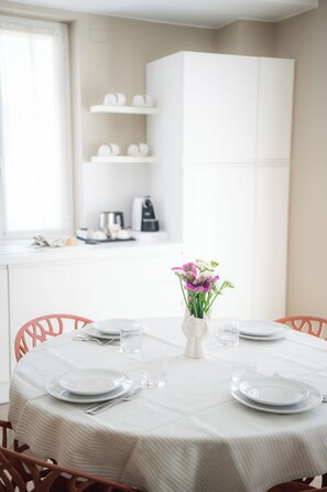A dining table set with plates, cutlery, and a vase of flowers, with a kitchen in the background. - Residence San Marco Suites&Apartments Alassio (Alassio)