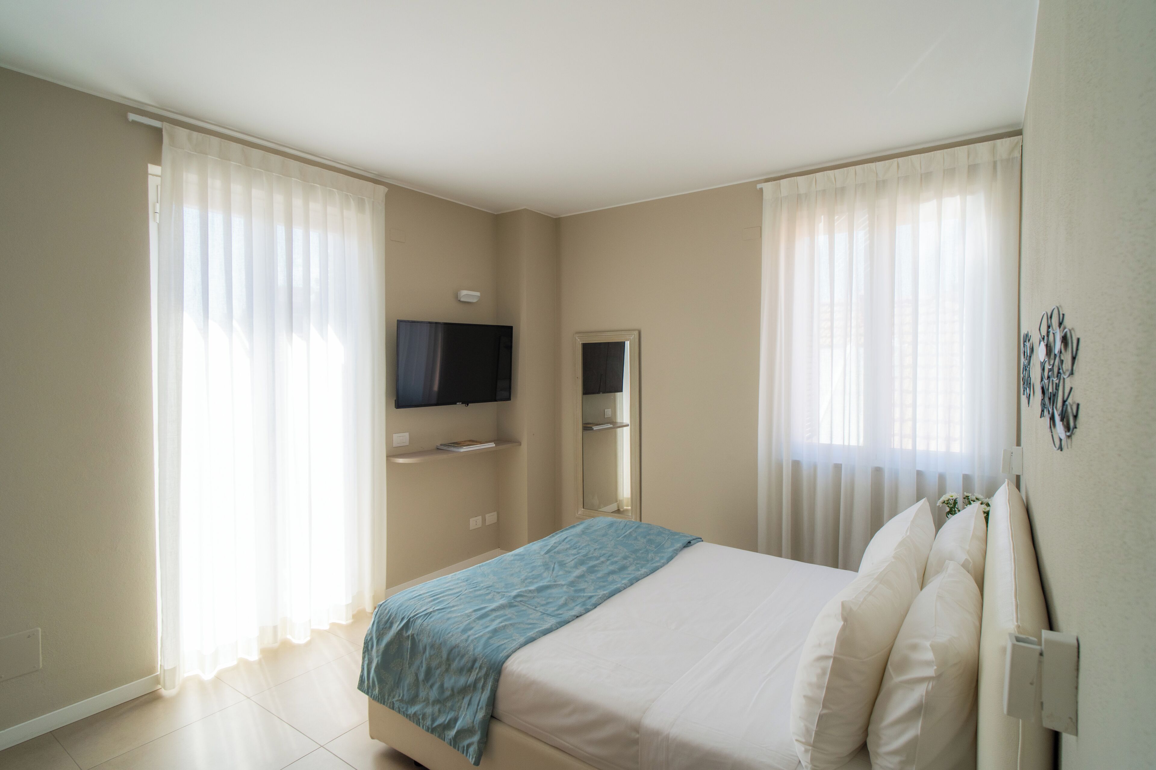 A hotel room with a bed, a TV mounted on the wall, and a window with curtains.