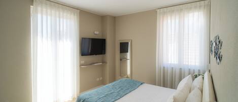 A hotel room with a bed, a TV mounted on the wall, and a window with curtains.