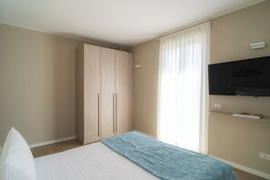 A bedroom with a bed, a wardrobe, a television, and a window with curtains. - Residence San Marco Suites&Apartments Alassio (Alassio)