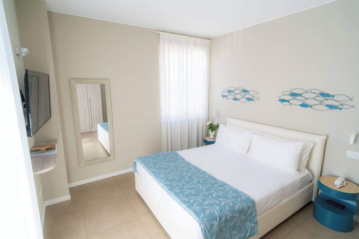 Une chambre d’hôtel comprenant un lit, une télévision, un miroir, une table de chevet avec une lampe et un élément décoratif mural.