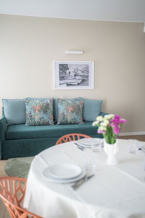 A dining area with a table set for four, a green sofa with patterned cushions, and a framed picture on the wall. - Residence San Marco Suites&Apartments Alassio (Alassio)