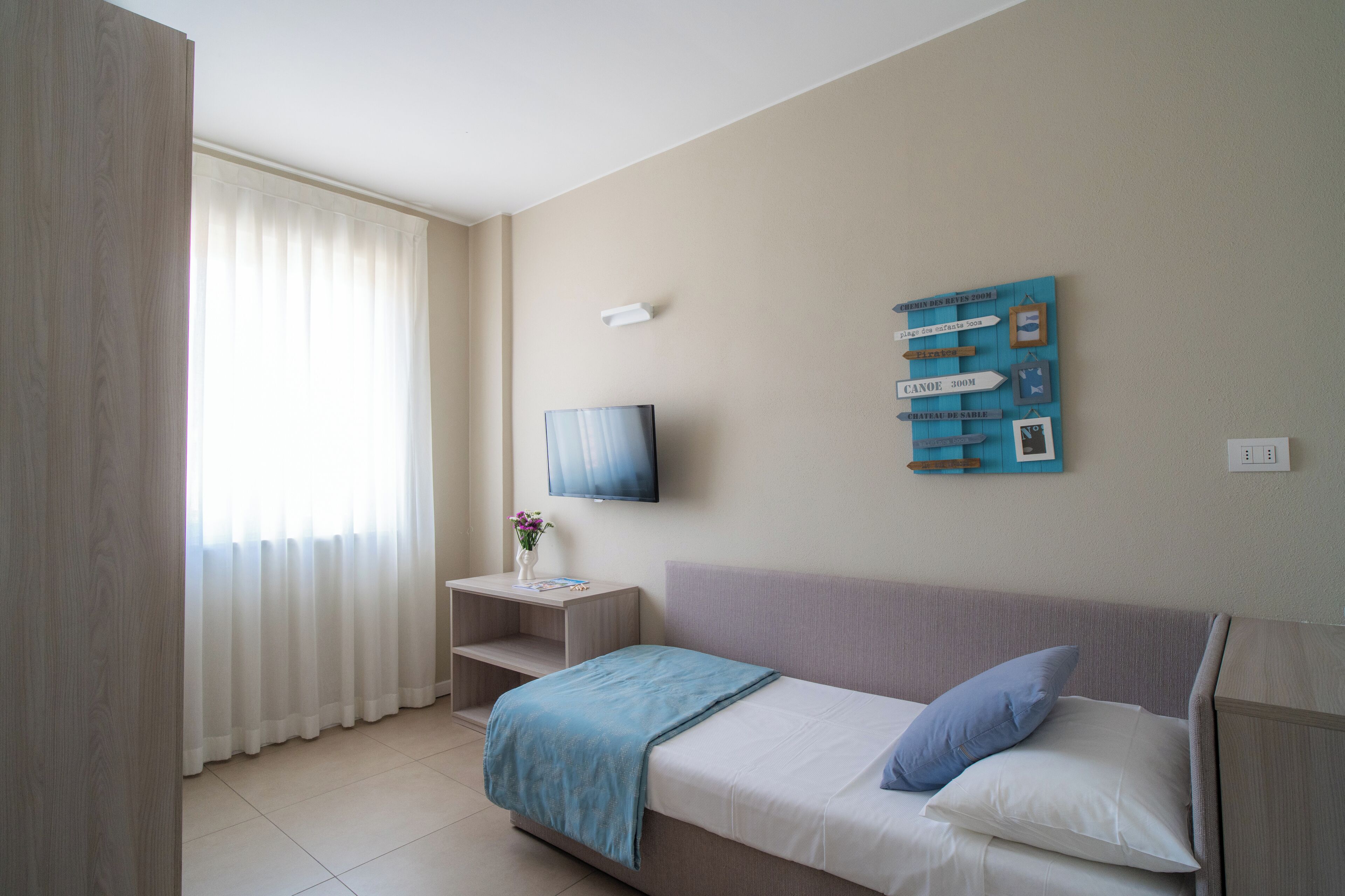A hotel room with a bed, a TV, a small table with a vase, and a wall with directional signs.