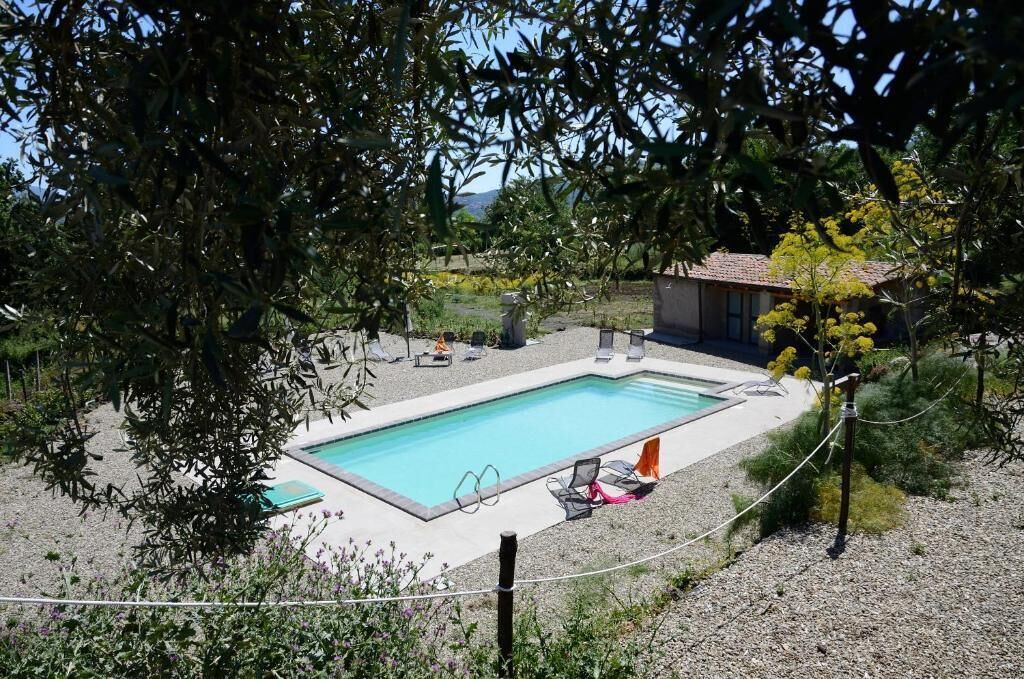 Ein rechteckiger Pool mit Liegestühlen und Sonnenschirmen, umgeben von Kies und Bäumen.