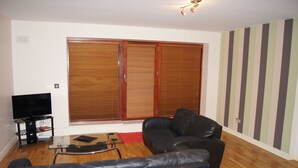 A living room with a black leather sofa, a glass coffee table, a flat-screen TV on a stand, and a wooden wardrobe with sliding doors. - Castleforbes Holiday Apartment (Dublin)