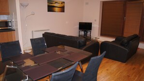 A living room with a sofa, a dining table with chairs, a TV, and a large window. - Castleforbes Holiday Apartment (Dublin)