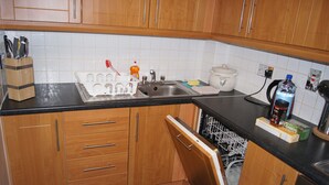 A kitchen with wooden cabinets, a black countertop, a dishwasher, and various kitchen appliances. - Castleforbes Holiday Apartment (Dublin)